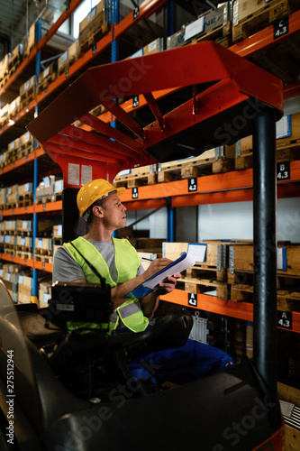Forklift operator examining stock of packages on shelves in a warehouse. © Drazen