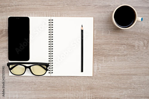 top view glasses,pencil and telephone place on open blank book,and coffee cup on wooden table.