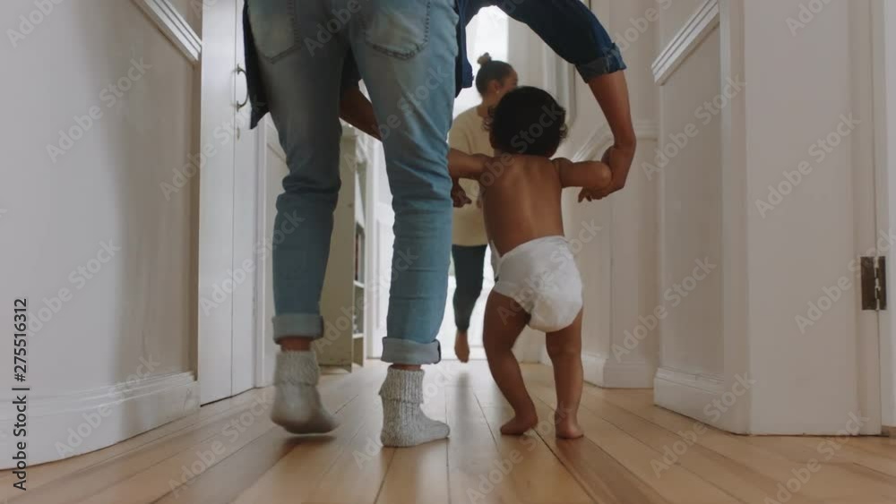 baby taking first steps learning to walk with mother and father teaching toddler at home enjoying parenthood