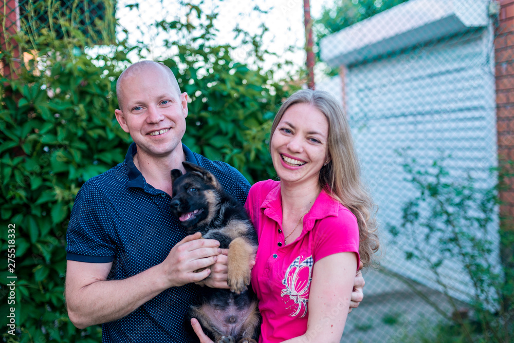 Young happy couple with a funny puppy of a German shepherd. A girl and a guy on a green lawn near the house with a new dog. Buying a pet. The joy of first meeting. Copy spase Young happy couple with a funny puppy of a German shepherd. A girl and a guy on a green lawn near the house with a new dog. Buying a pet. The joy of first meeting. Copy spase
