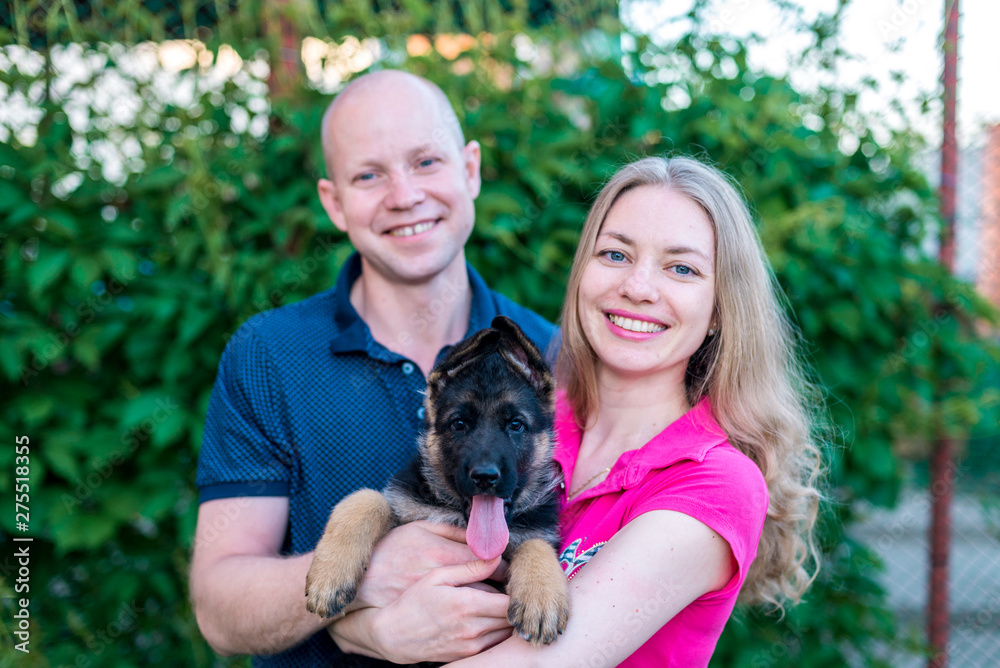 Young happy couple with a funny puppy of a German shepherd. A girl and a guy on a green lawn near the house with a new dog. Buying a pet. The joy of first meeting. Copy spase Young happy couple with a funny puppy of a German shepherd. A girl and a guy on a green lawn near the house with a new dog. Buying a pet. The joy of first meeting. Copy spase