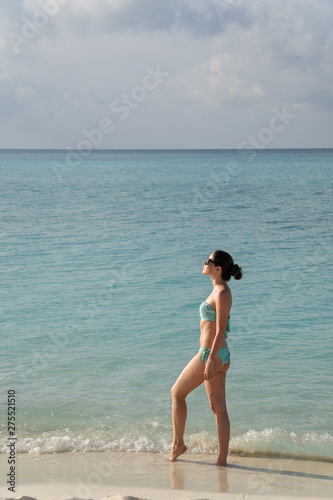 A young girl is beautifully standing in a bathing suit at the water's edge and basking in the sun. © Raman