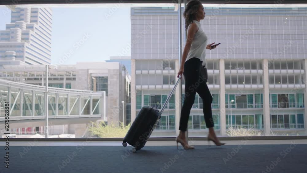 young business woman traveler walking using smartphone pulling trolly bag in airport texting checking messages female commuter traveling international for business trip 4k