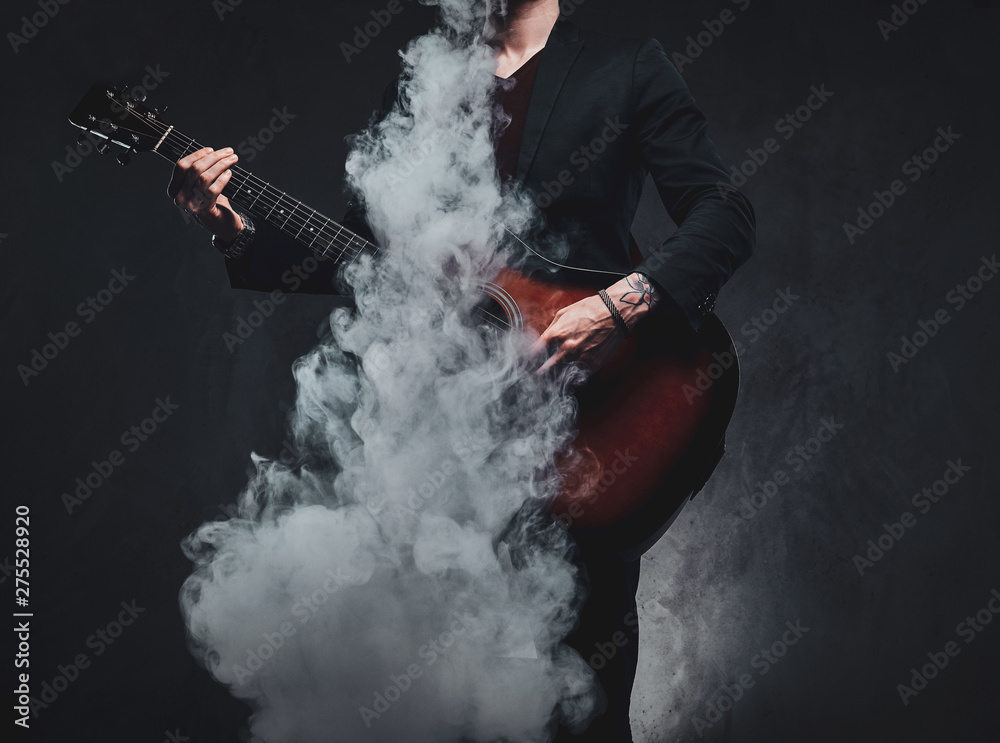 Obraz premium Młody atrakcyjny mężczyzna gra na gitarze akustycznej podczas palenia vape, robiąc wielką mgiełkę.