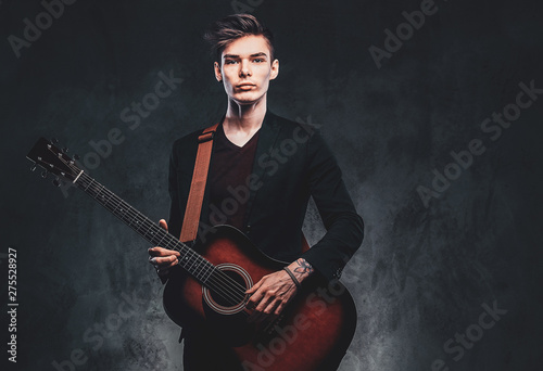 Young attractive man is playing acoustic guitar at studio while posing for photographer.