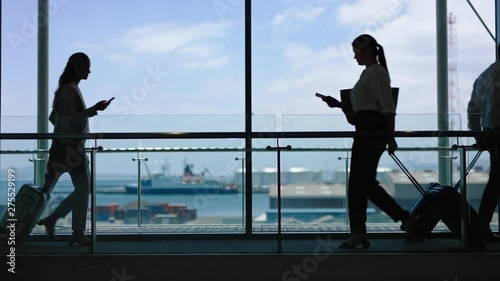 business people at busy airport pulling trolley bags arriving and departing terminal tourists travelling international walking in lobby with view of harbor port 4k footage