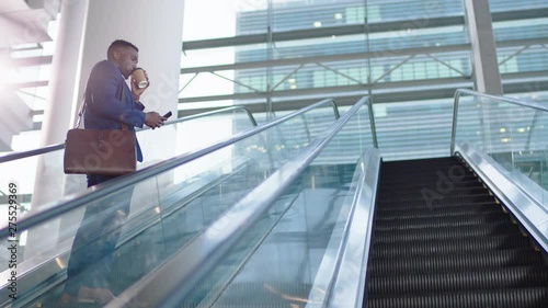 young african american businessman using smartphone on escalator texting drinking coffee checking email messages successful male executive arriving at work in corporate office building 4k