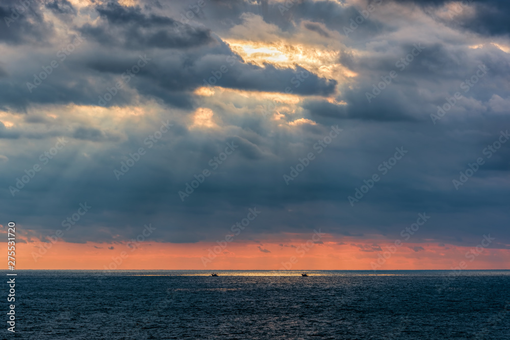 Incredible sunset over sea with a silhouettes of a small fishing ship.