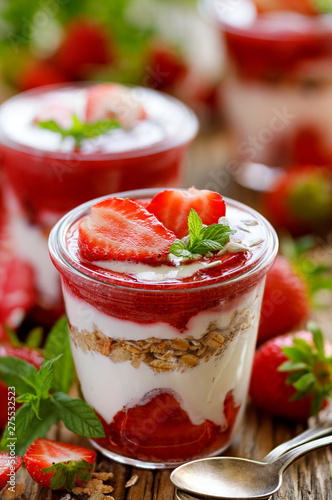 Strawberry layered dessert  healthy dessert with fresh strawberries  natural yoghurt  strawberry mousse and granola in glass dishes on a wooden table. Delicious and nutritious dessert or breakfast