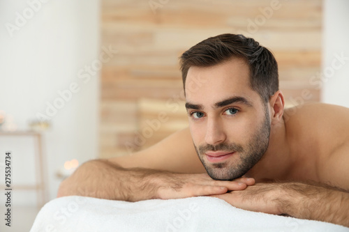 Handsome man relaxing on massage table in spa salon. Space for text