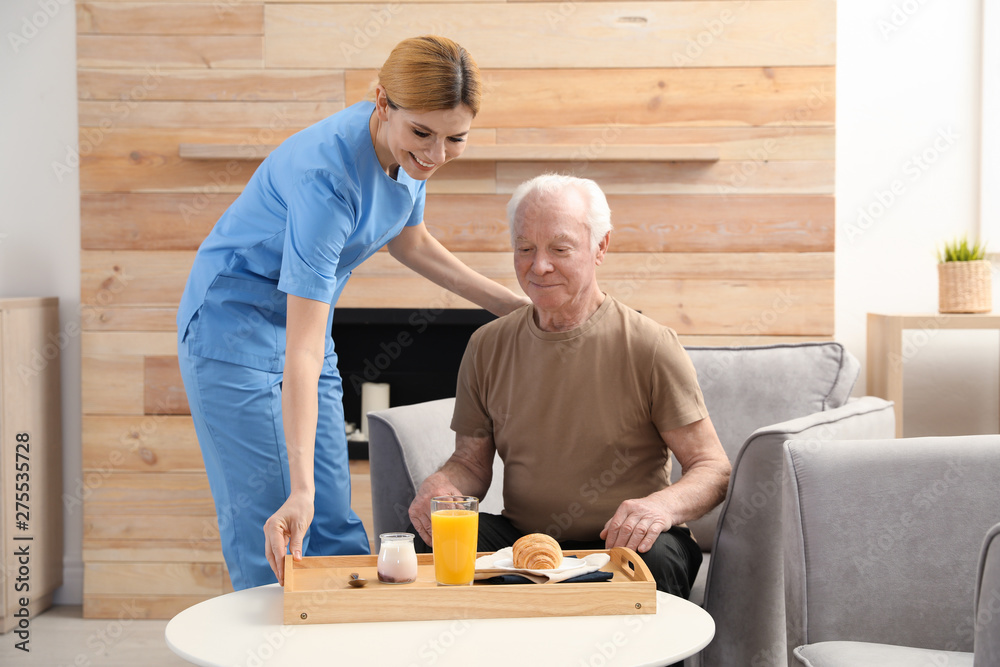 Nurse serving breakfast to elderly man indoors. Assisting senior people Nurse serving breakfast to elderly man indoors. Assisting senior people