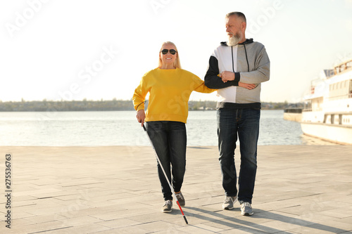 Mature man helping blind person with long cane in city