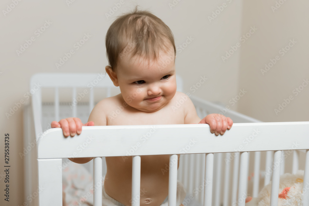 Baby girl in a diaper playing in the crib.