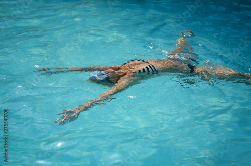Young girl floating and swimming on pool water .
