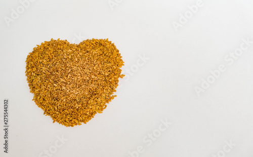 Top view on pile of golden flax seeds. Linseeds in heart shape isolated on white background with copy space. Healthy food for preventing heart diseases, cancer and overweight.
