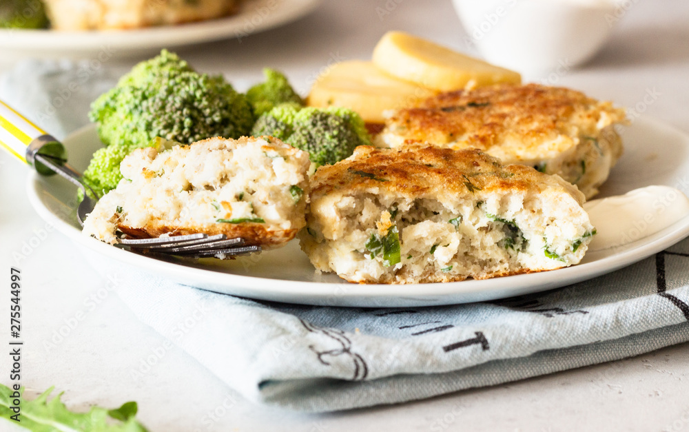 Delicious cutlets (fish or meat) with broccoli, potatoes and sauce on a plate. Light grey stone background. 