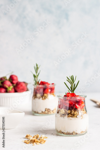 Breakfast with yogurt, granola and fresh strawberry in a mason jar on a light stone background. Healthy breakfast or dessert concept, selective focus. Copy space.