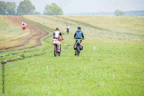 Group of travelling bikers with backpacks on dirty rural road after rain. Summer landscape with green hills