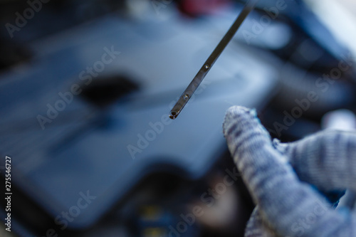 Close-up car mechanic's hands in gray gloves holding dipstick of oil level in the engine. Auto mechanic checks oil level in car engine with finger pointing the correct oil level.