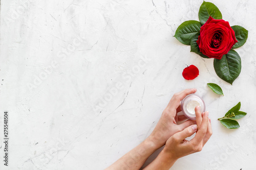 Cream in hands for organic cosmetics with rose flower on white marble background top view space for text