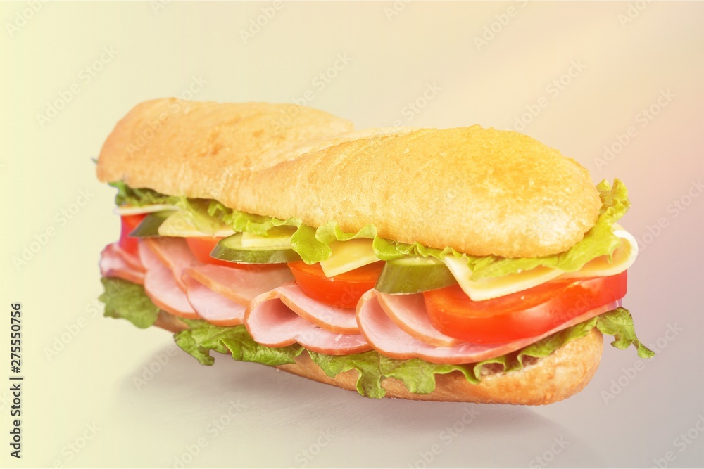 Long baguette sandwich with lettuce, vegetables, ham, and cheese on white background Long baguette sandwich with lettuce, vegetables, ham, and cheese on white background