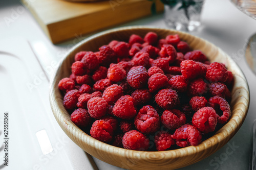 Ripe raspberries in a wooden plate on the table