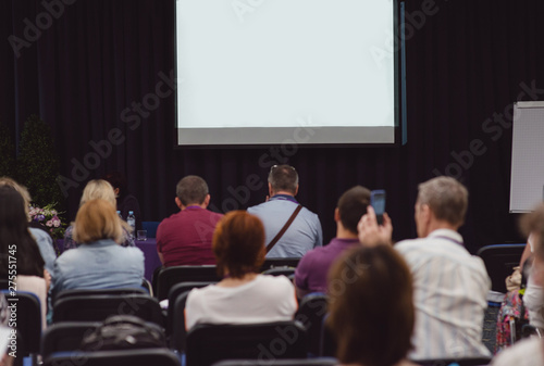 A big white screen without text. A conference concept. People sitting and watching blank screen for presentation and waiting a speaker. A screen with copy space.