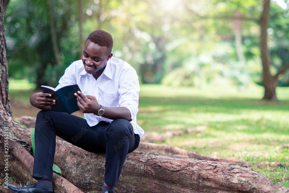 African man reading a book in the park.