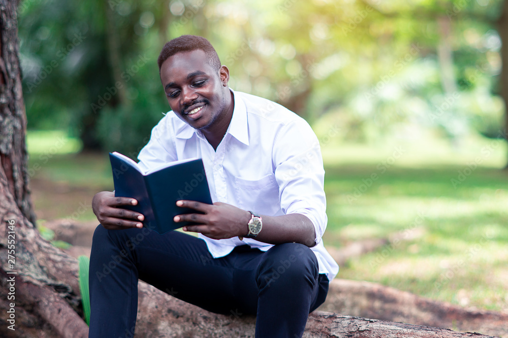 African man reading a book in the park. African man reading a book in the park.
