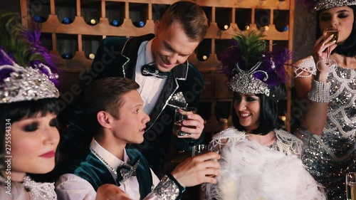 Theme party - young people in glistening retro clothes sitting behind the table and drinking alcohol photo