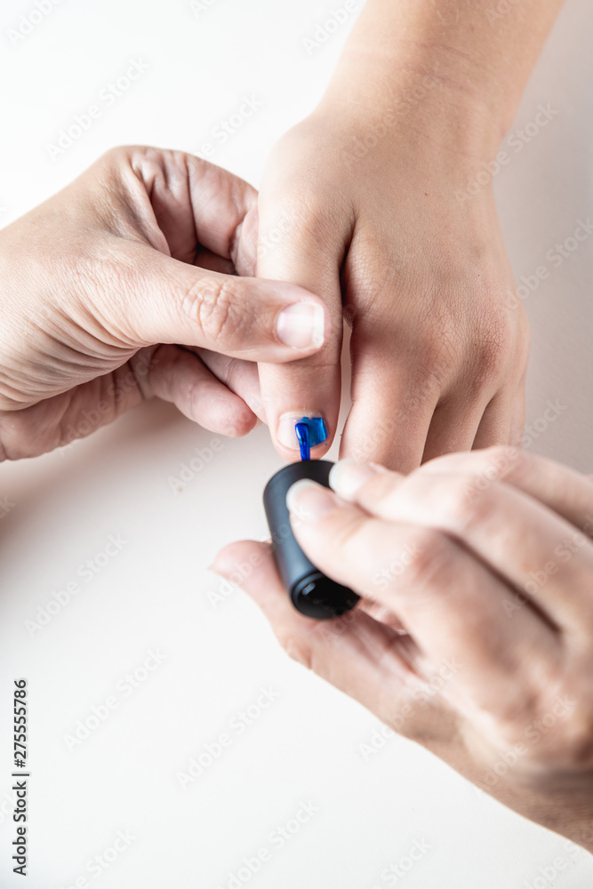A mother paints her young girl's hands with blue and pink nailpolish, viewed against an isolated white background A mother paints her young girl's hands with blue and pink nailpolish, viewed against an isolated white background