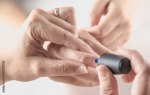A mother paints her young girl's hands with blue and pink nailpolish, viewed against an isolated white background