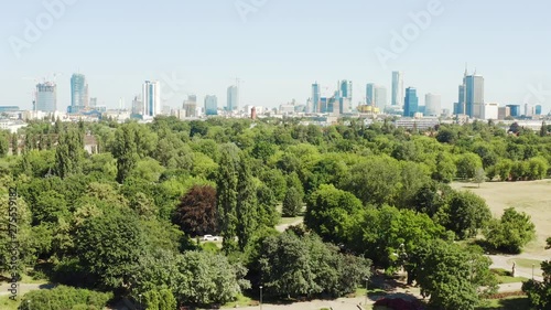 Warsaw cityscape with central park, aerial landscape with skyscrapers. Aerial view of trees and a lake with fantans, Park Mokotovo Field to downtown Warsaw / Poland, bright day lighting. 4K Drone Shot photo