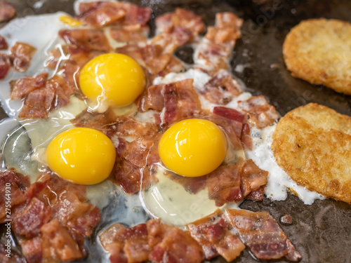 sizzling fried eggs with bacon and hash browns on a skillet.