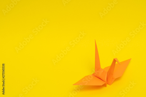 orange origami paper crane on yellow background
