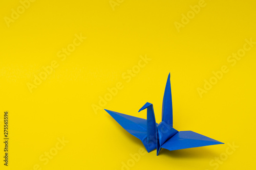 blue origami paper crane on yellow background