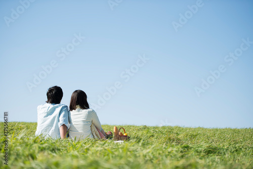 草原でピクニックをするカップルの後ろ姿 © ohayou!