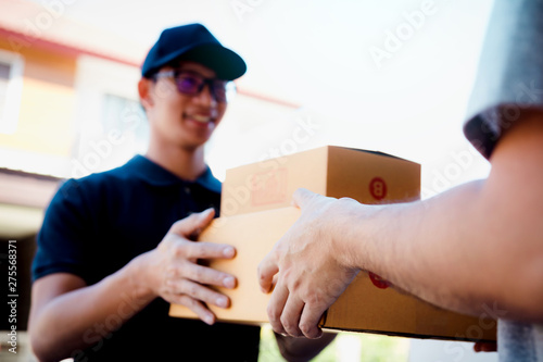 Asian cargo carrier holds a cardboard box with the package inside and the recipient is signing the package.
