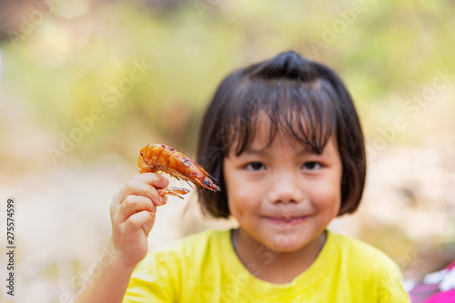 Little Asian girl holding a piece of grilled shrimps