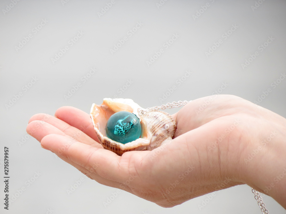 Seashell and sphere pendant in hand