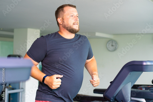 chubby man walking on running track, warming up on gym treadmill.