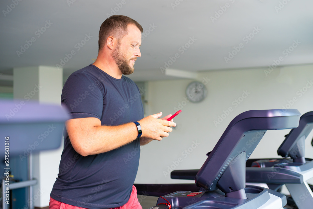 chubby man walking on running track, warming up on gym treadmill. man with phone chubby man walking on running track, warming up on gym treadmill. man with phone