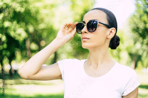 Stylish trendy young beautiful woman in sunglasses portrait. Woman in city park is posing