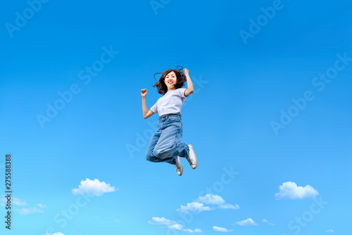 青空を背景にジャンプする女性。幸せ、飛躍、未来イメージ