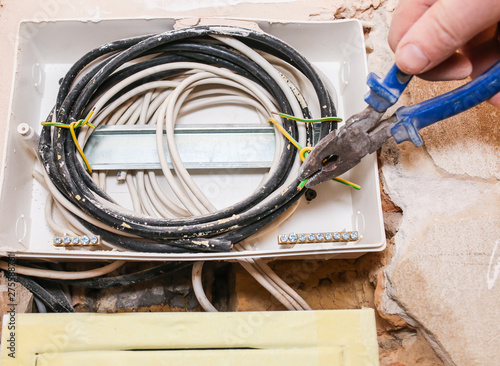 Worker is cutting wires with lineman's pliers. Electrical panel. Maintenance repair works renovation in the flat. Restoration indoors. photo