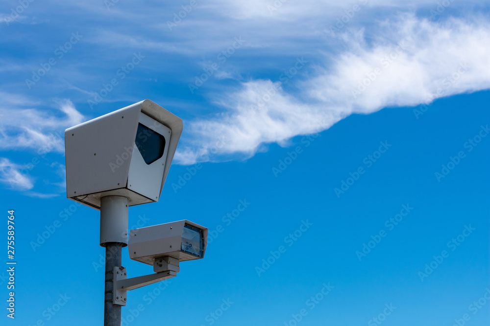 Red light camera. Close up. Traffic enforcement camera. Background blue sky with light clouds during day time. Red light camera. Close up. Traffic enforcement camera. Background blue sky with light clouds during day time.