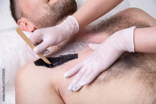 Closeup of male chest with hair and wax. Professional shugaring master in gloves makes depilation to a young man in the salon