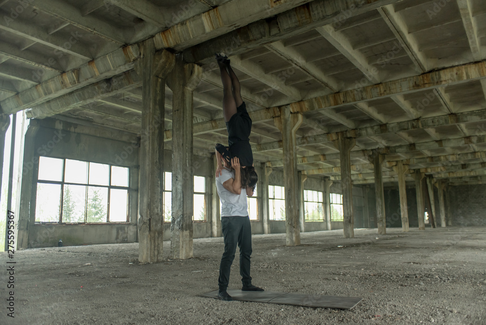 A young girl and boy perform acrobatic moves in the premises of an old factory, a warehouse, acro 