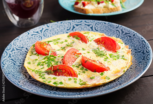 Omelette with tomatoes, ham and green onion on dark table. Frittata - italian omelet.