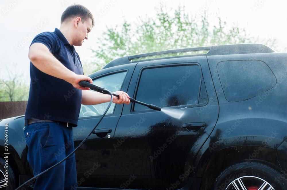 A man washes a black car from a hose with high-pressure water near the garage A man washes a black car from a hose with high-pressure water near the garage